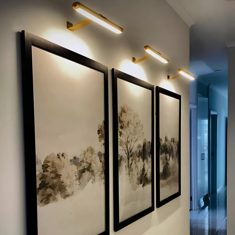 Gold cordless picture lights above three framed ink paintings in a hallway | Casa Norex