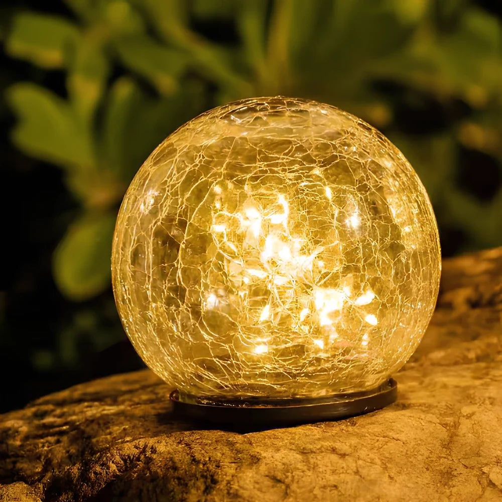 Close-up of a large cracked glass solar globe glowing on a mossy stone | Casa Norex