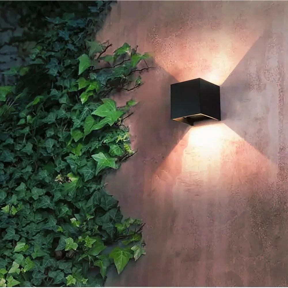 Black cube wall light on a textured wall beside climbing ivy — Casa Norex