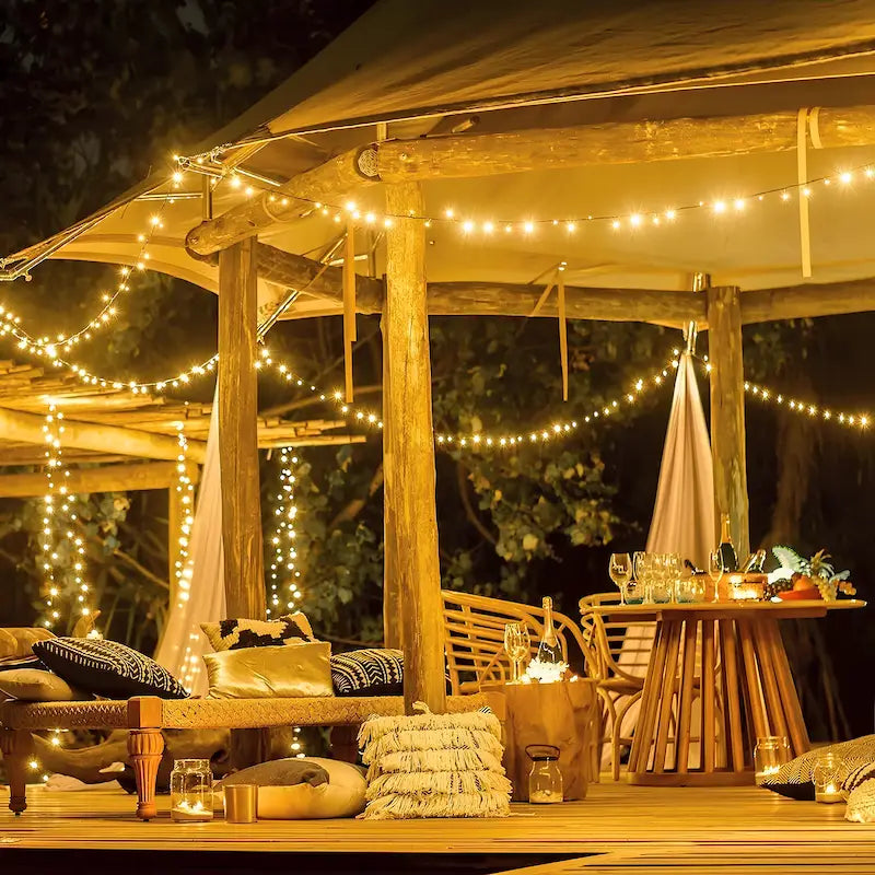 Warm white fairy lights strung across a garden pergola and seating area — Casa Norex