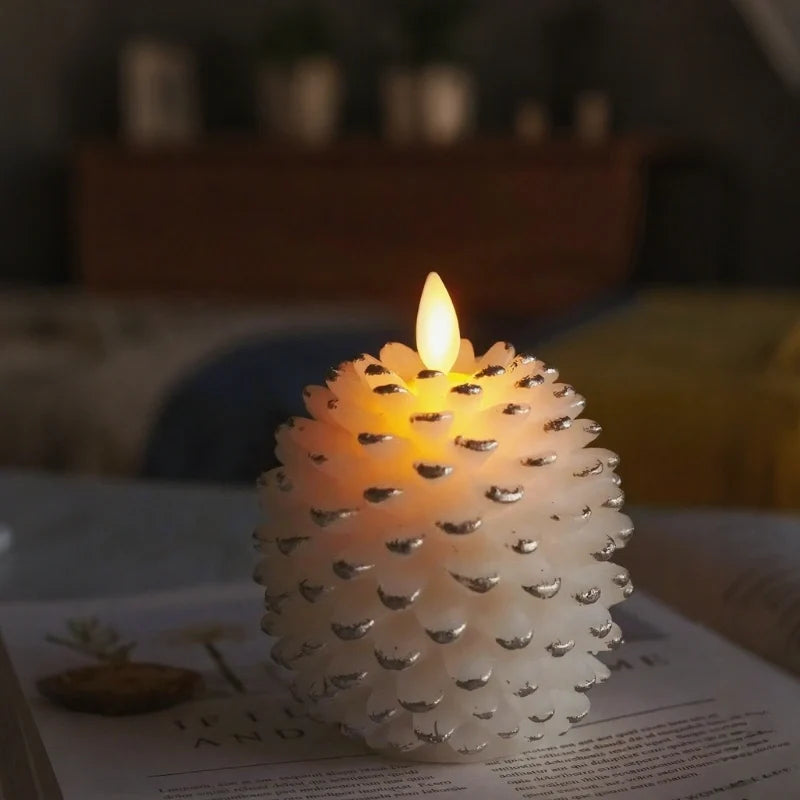 White pinecone flameless candle glowing in a dim room, silver-tipped scales and flickering flame — Casa Norex