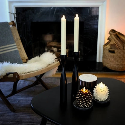 Pinecone flameless candles in gold-brown and white beside taper candles on a black table by a fireplace — Casa Norex