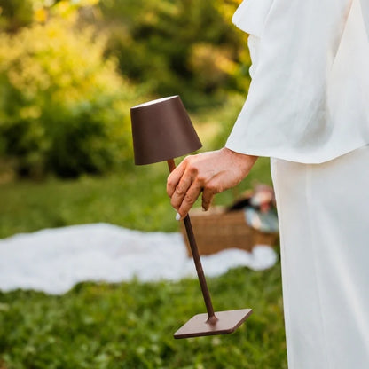 Hand placing a brown table lamp on a lawn picnic setting — Casa Norex
