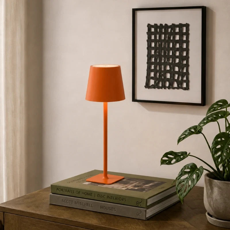 Matte orange table lamp on a stack of books by a framed print — Casa Norex