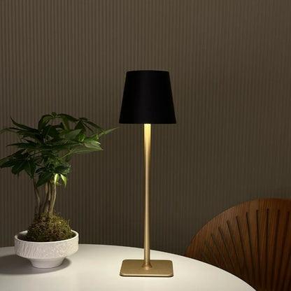 Black table lamp with a gold base on a round table by a plant — Casa Norex