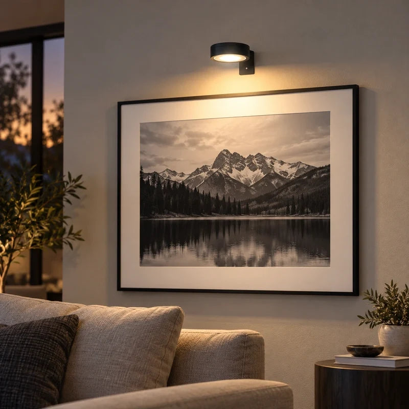 Black cordless picture light over a framed mountain lake photograph
