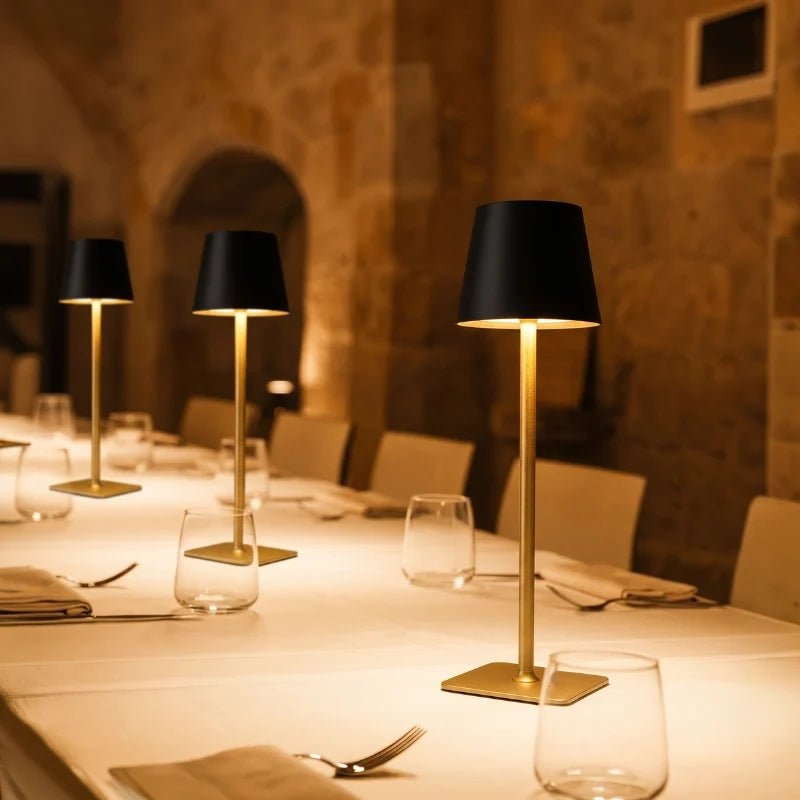 Gold and black table lamps lit along a long stone-room dining table — Casa Norex