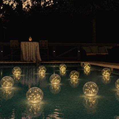 Floating solar lights on a pool at night with a terrace table beyond