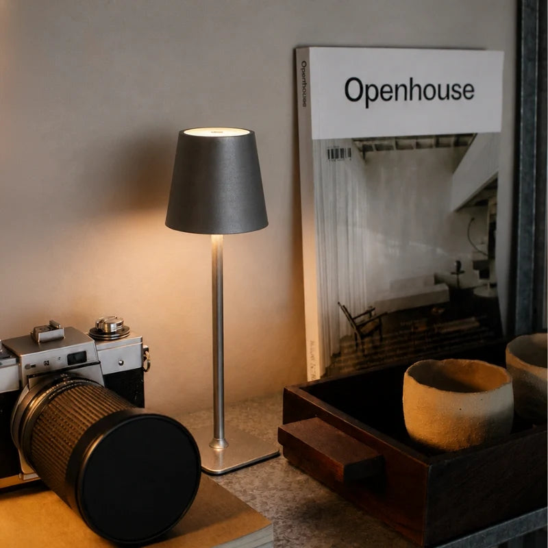 Dark grey table lamp on a desk beside a camera and magazine — Casa Norex
