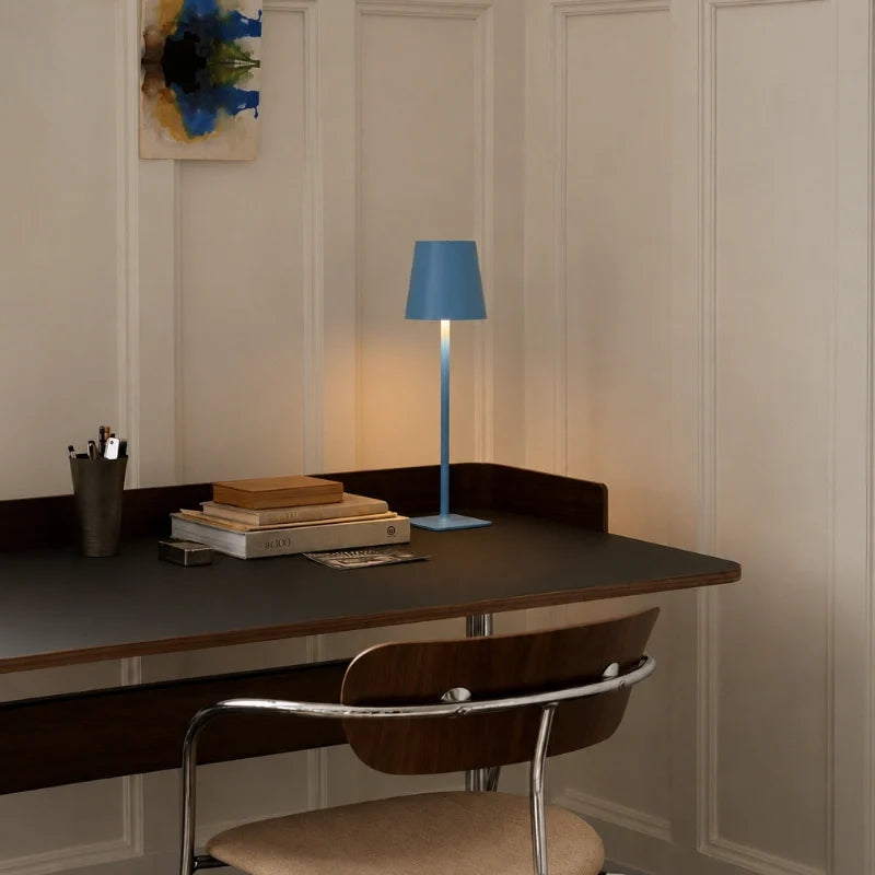 Matte blue cordless lamp glowing on a dark desk beside books — Casa Norex