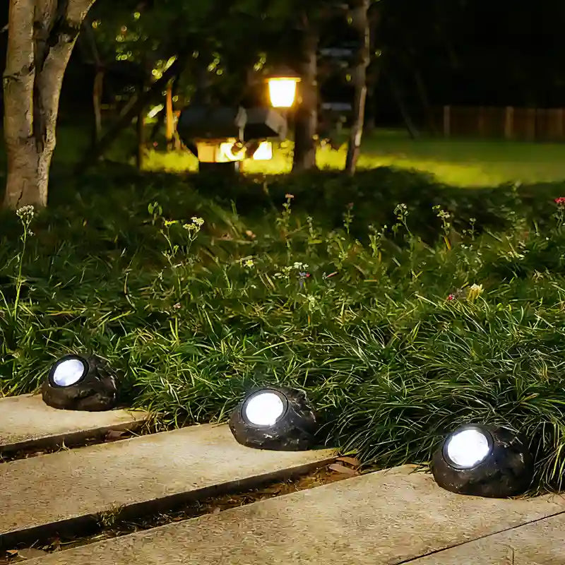 Solar stone lights on a lawn edge beside a stone path at dusk