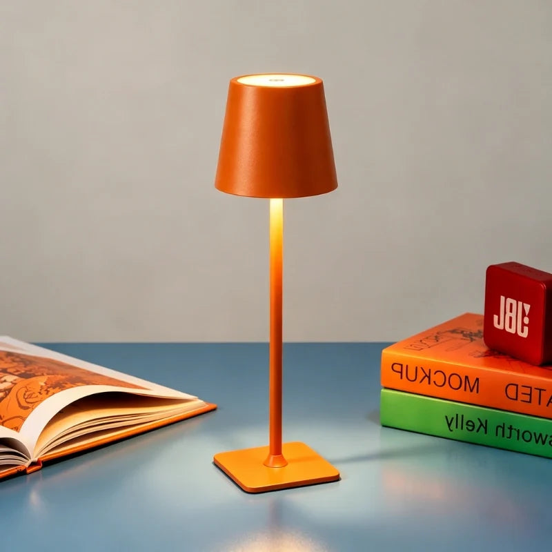 Matte orange table lamp on a blue table beside open books — Casa Norex