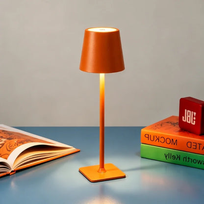 Matte orange table lamp on a blue table beside open books — Casa Norex