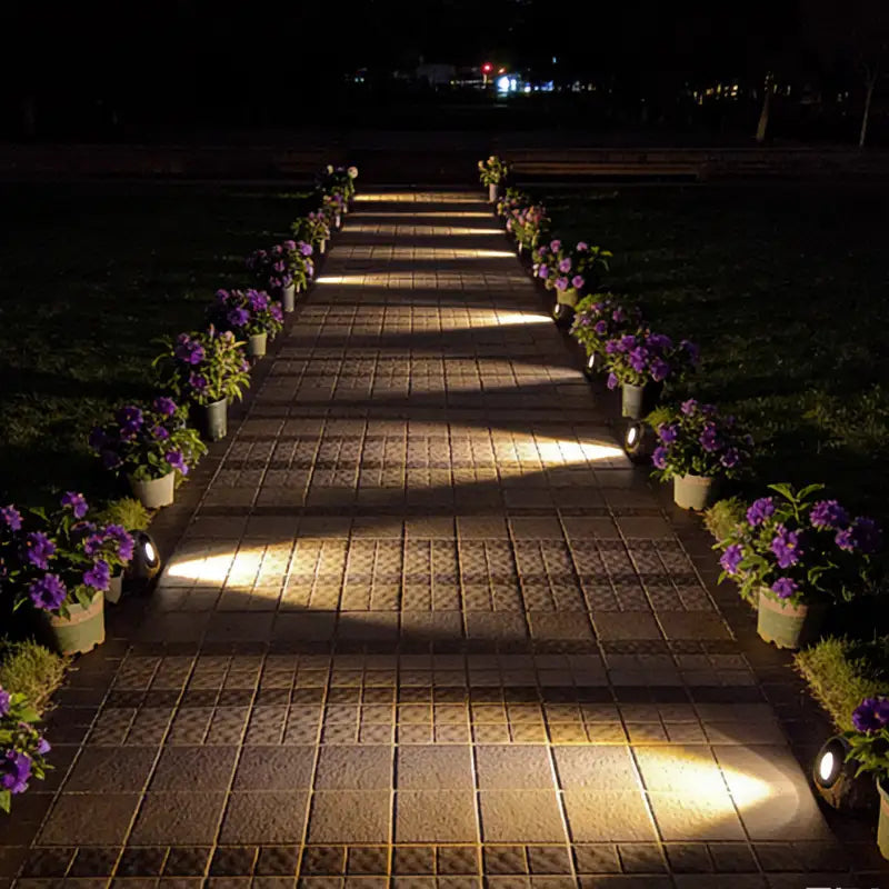 Solar path lights glowing along a paved walkway lined with purple flowers