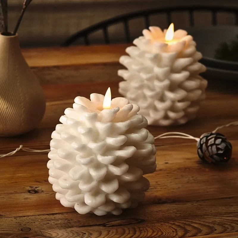 Two white pinecone candles with lit LED flames on a wooden table beside a vase | Casa Norex