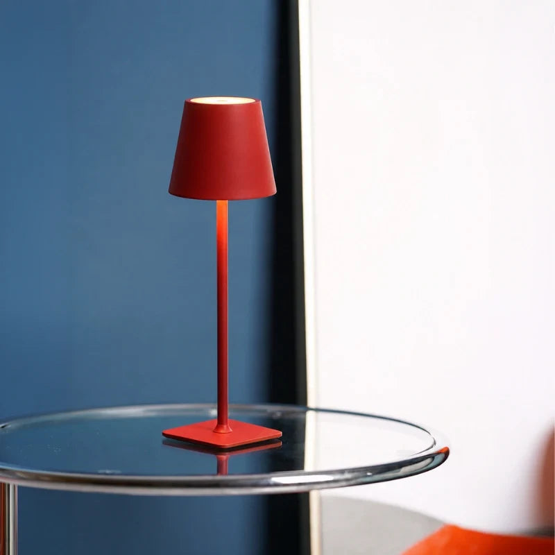 Matte red table lamp on a glass side table against a blue wall — Casa Norex