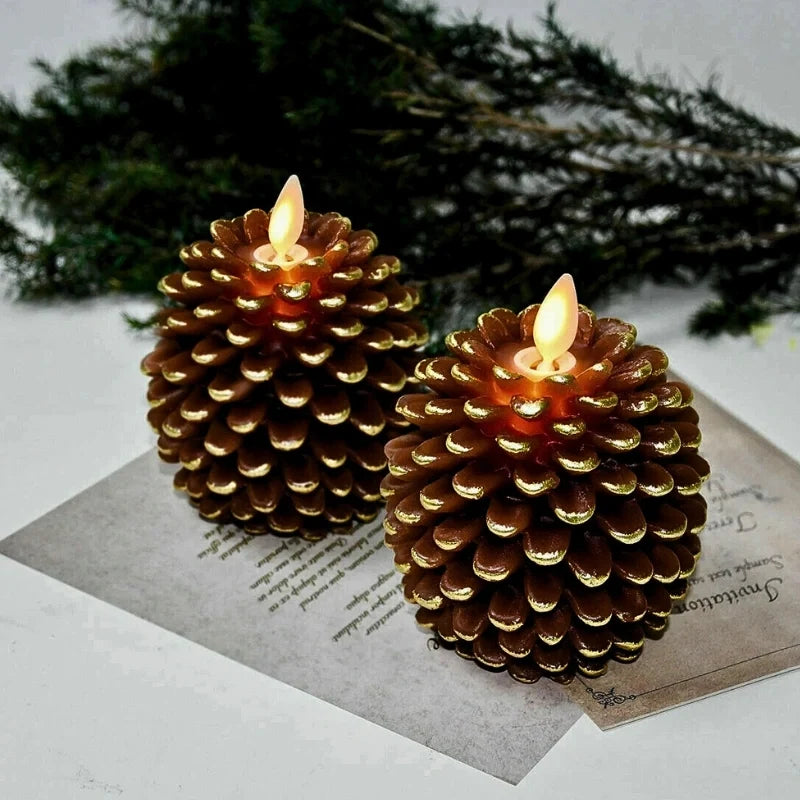 Two golden brown pinecone candles with lit flames on printed paper with evergreen branches behind — Casa Norex