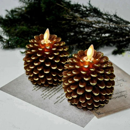 Two golden brown pinecone candles with lit flames on printed paper with evergreen branches behind — Casa Norex