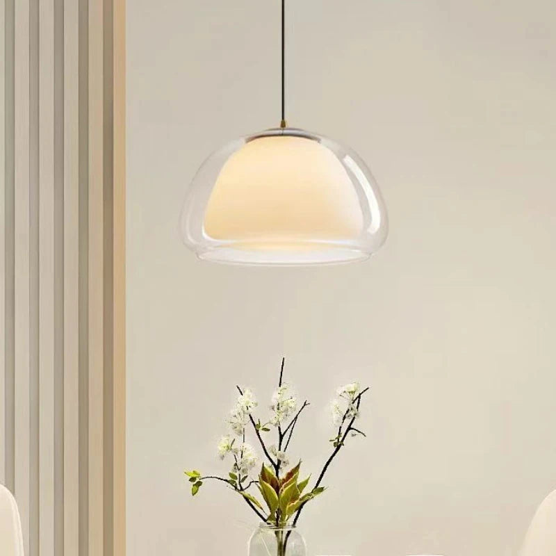Double glass pendant light glowing above a vase of white flowers — Casa Norex