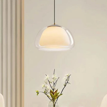Double glass pendant light glowing above a vase of white flowers — Casa Norex