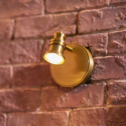 Single-head brass wall sconce lit on a red brick wall — Casa Norex