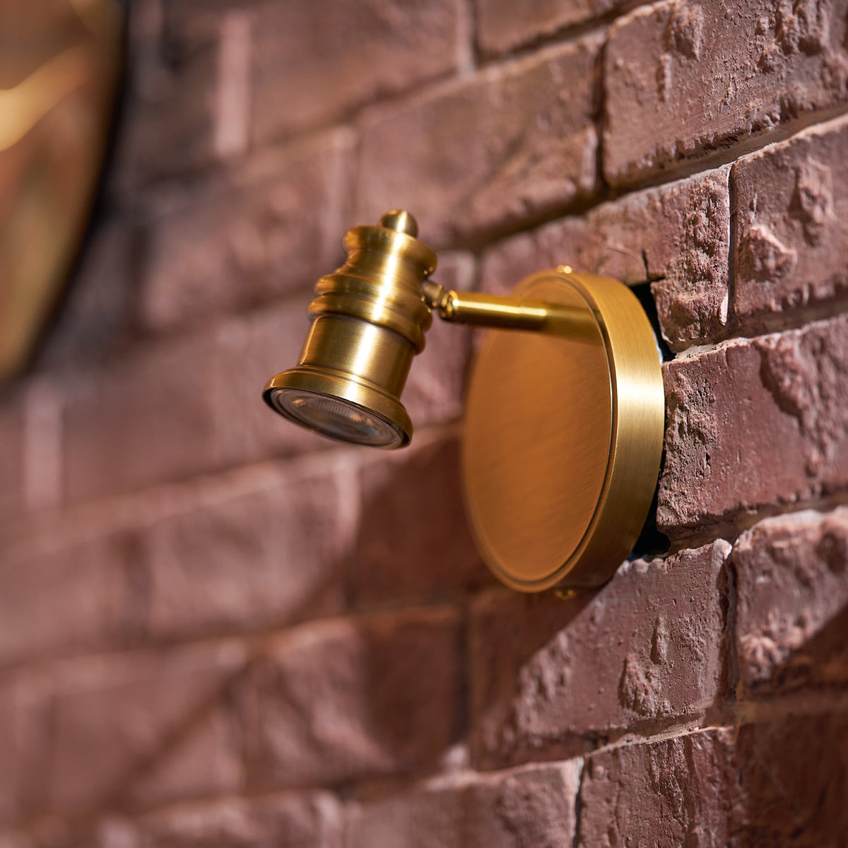 Single brass spotlight head angled on a red brick wall — Casa Norex