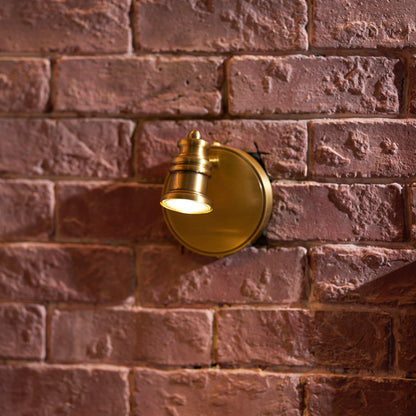 Single-head brass wall sconce glowing against textured brick — Casa Norex