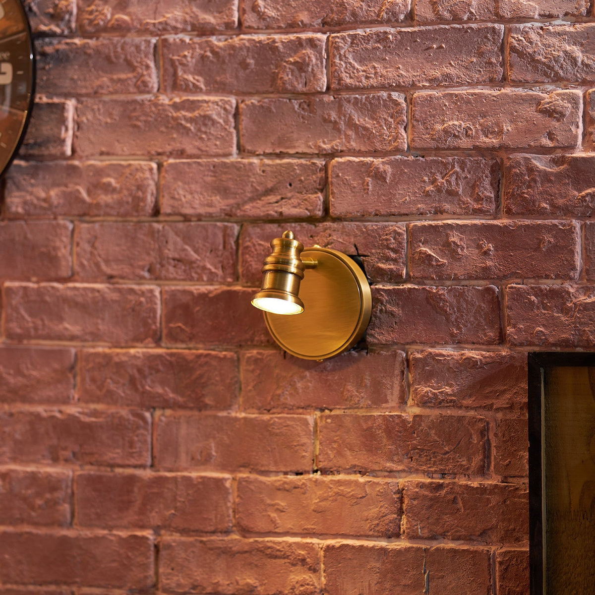 Small brass wall sconce on a red brick wall in a living space — Casa Norex