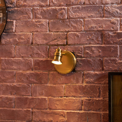 Small brass wall sconce on a red brick wall in a living space — Casa Norex