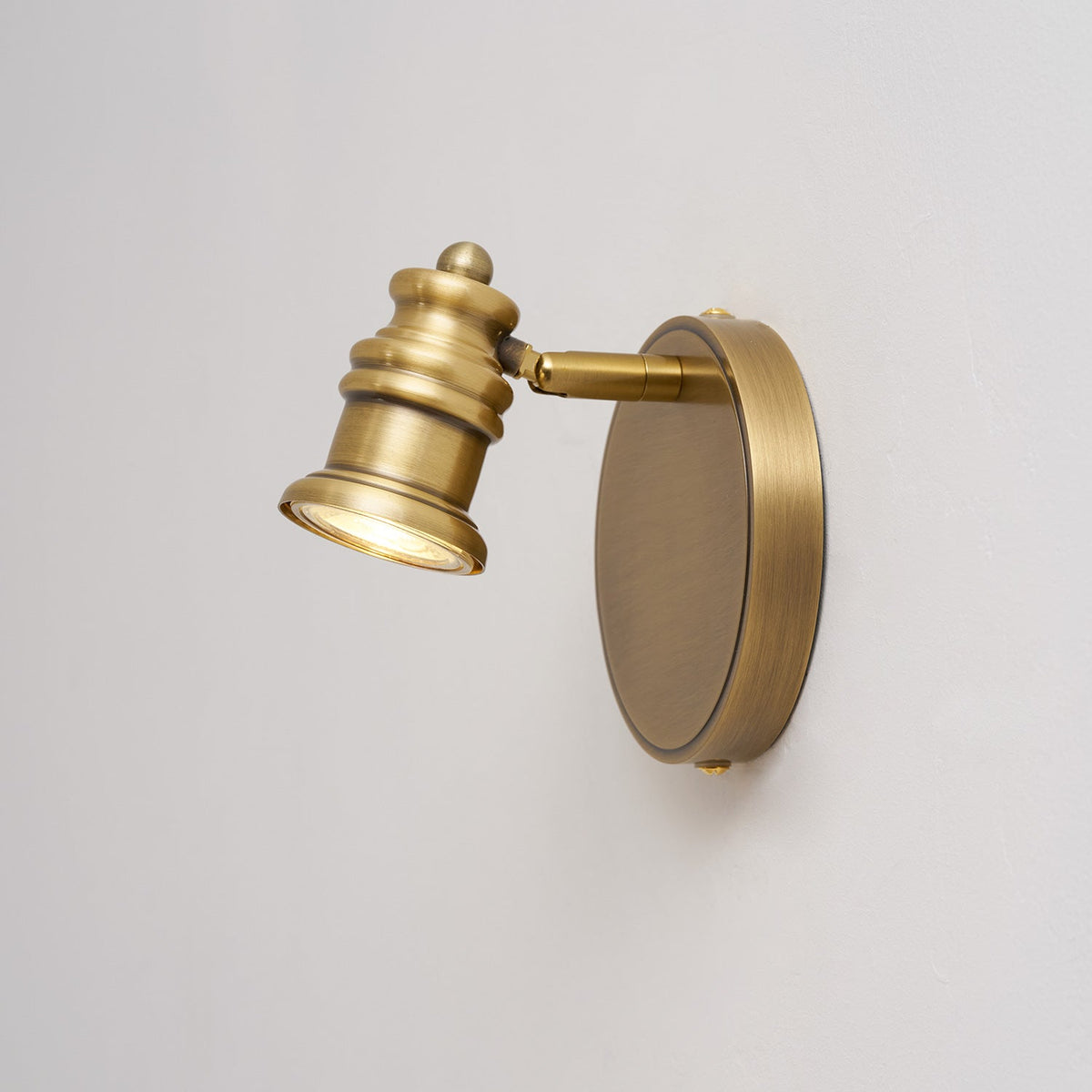 Side view of a single brass spotlight head on a round backplate — Casa Norex