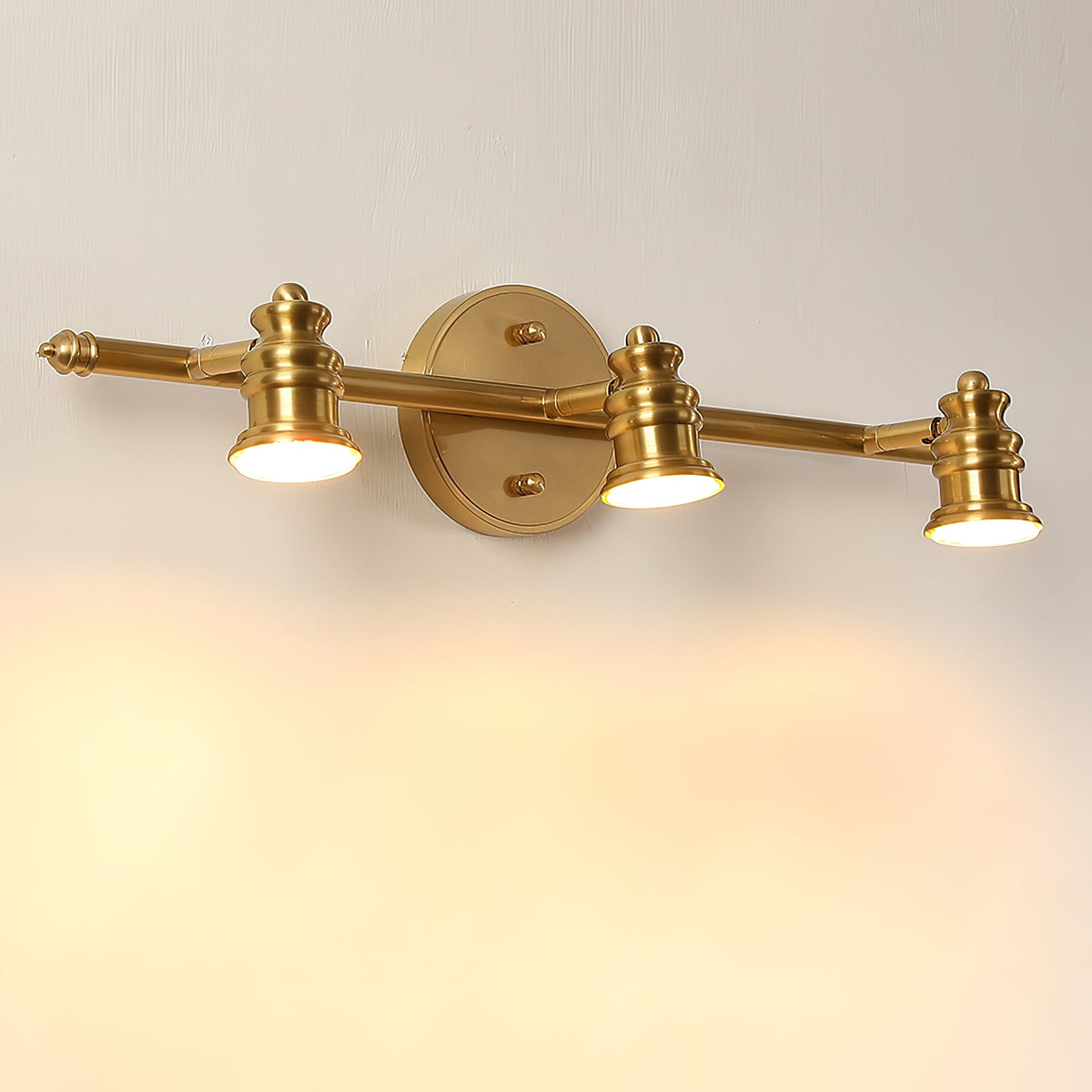 Three-head brass spotlight bar glowing warmly on a cream wall — Casa Norex