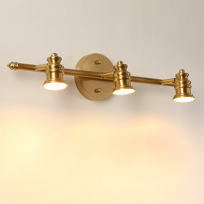 Three-head brass spotlight bar glowing warmly on a cream wall — Casa Norex