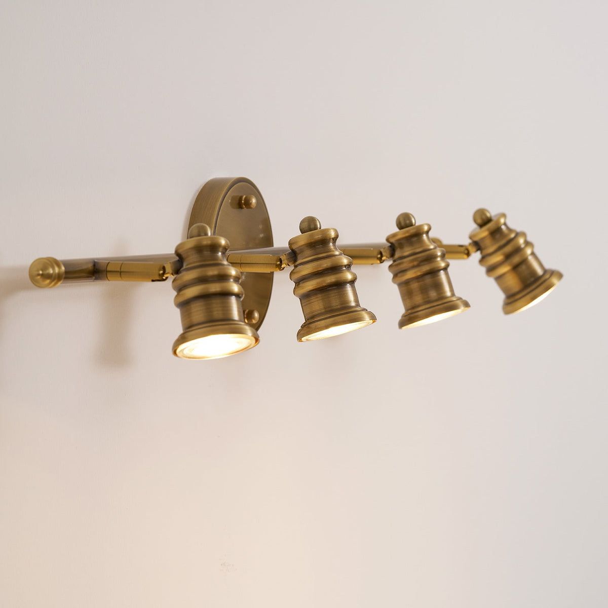 Four-head brass spotlight bar wall sconce lit in warm light — Casa Norex