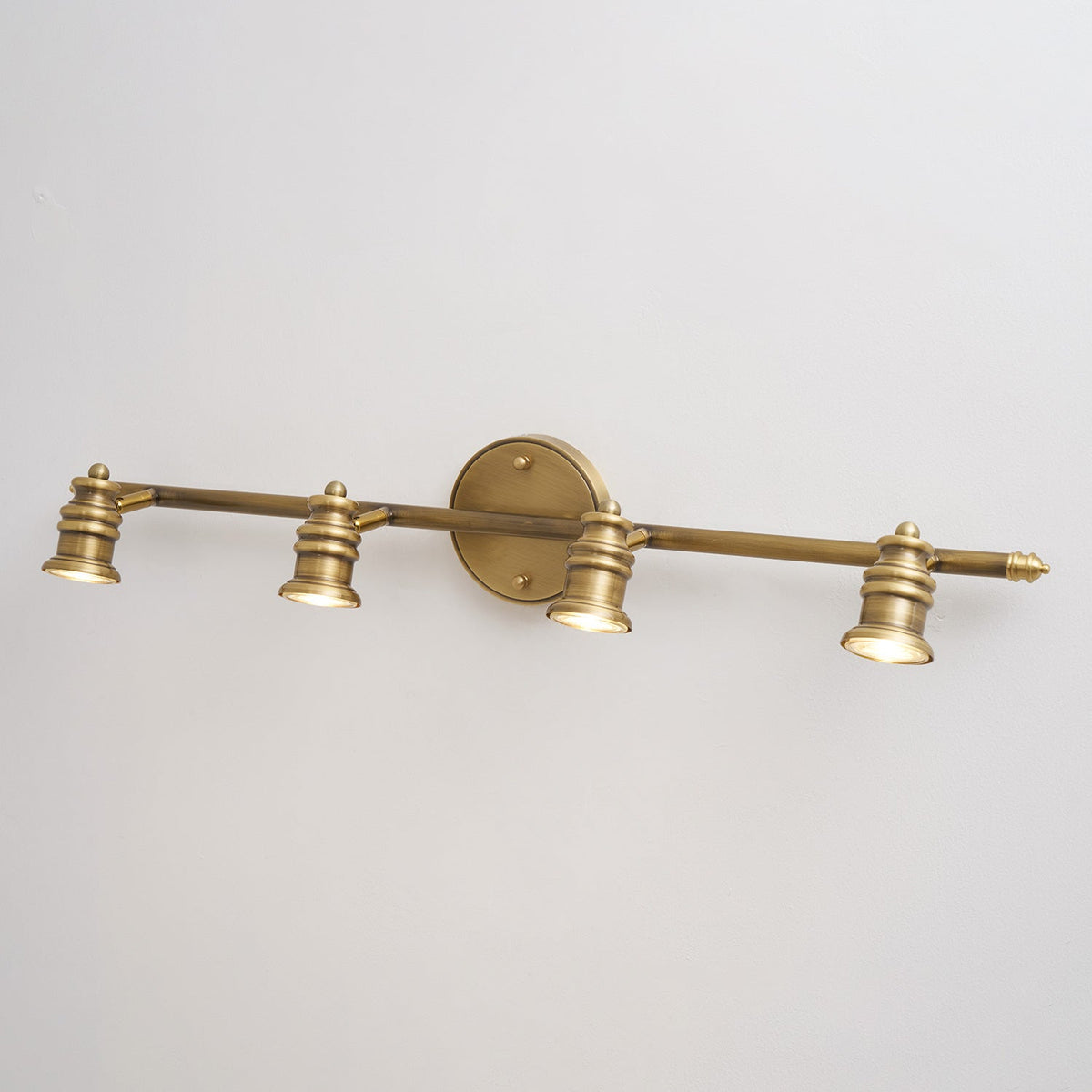 Three-head brass spotlight bar on a white wall, front view — Casa Norex