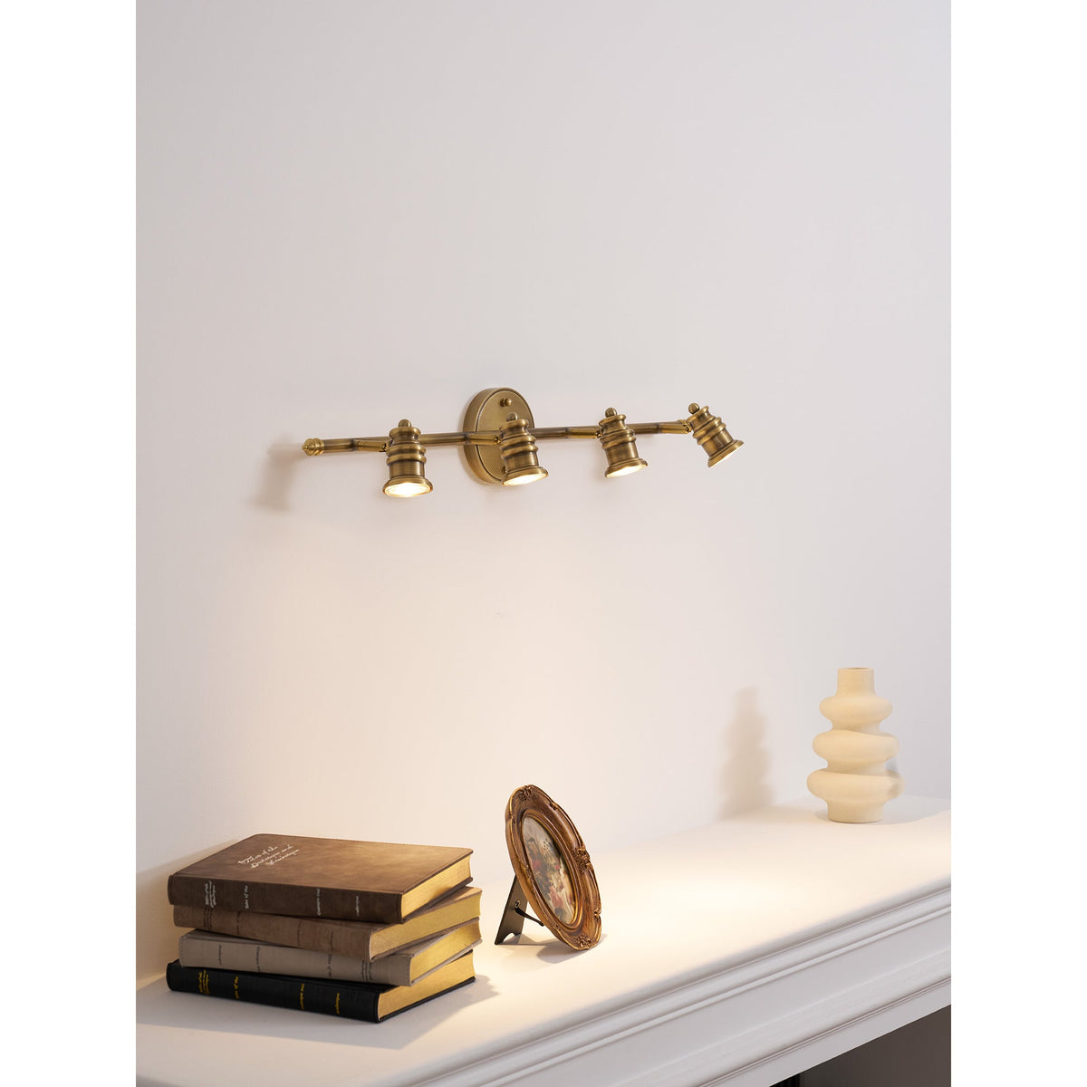 Three-head brass spotlight bar above a shelf with books — Casa Norex