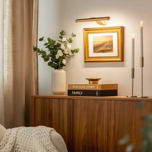 Gold cordless picture light above a framed painting on a wooden console | Casa Norex