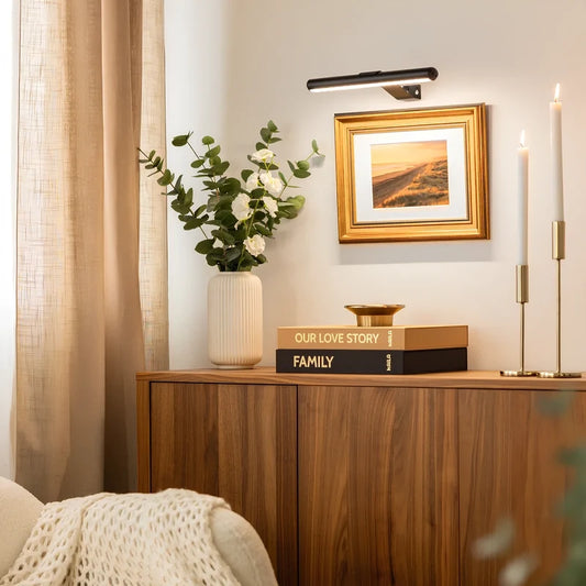 Black cordless picture light above a framed painting beside candlesticks | Casa Norex