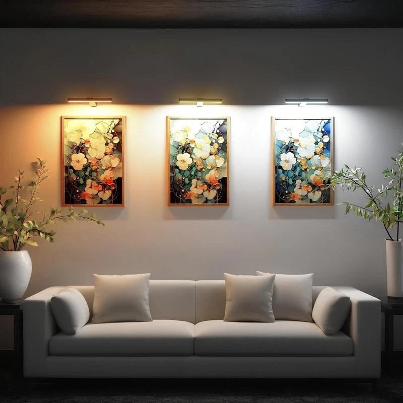 Three cordless picture lights above floral paintings over a sofa — Casa Norex