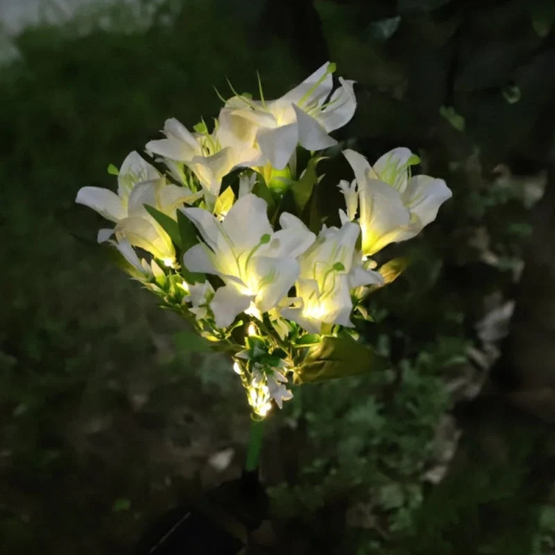 White lily stake lights lit warm white against dark foliage | Casa Norex