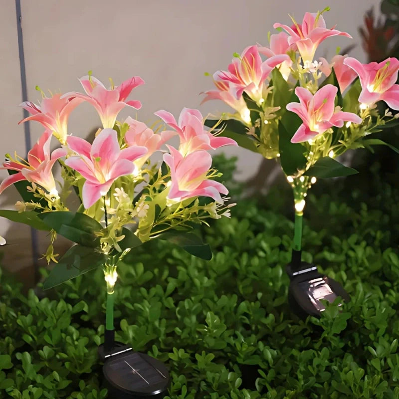 Pink lily stake lights with a solar panel stake in a garden bed — Casa Norex