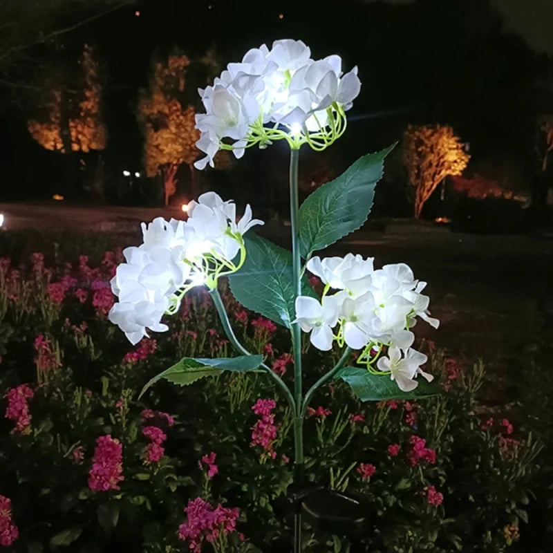 White hydrangea stake lights lit cool white in a garden at night — Casa Norex