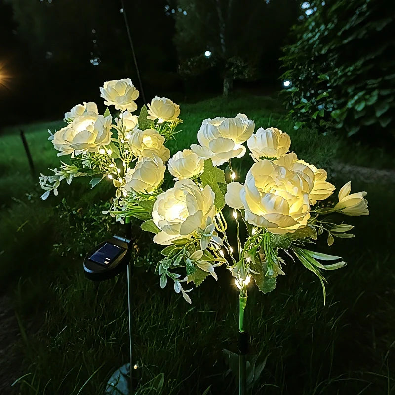 Cream peony stake lights glowing in a garden bed at night — Casa Norex