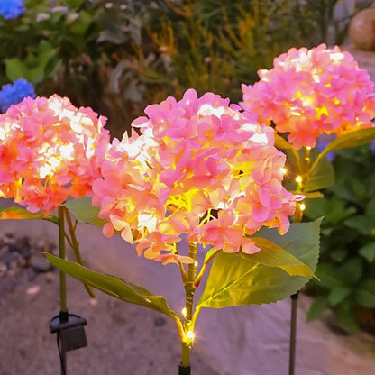 Pink hydrangea stake lights glowing in a garden at night — Casa Norex