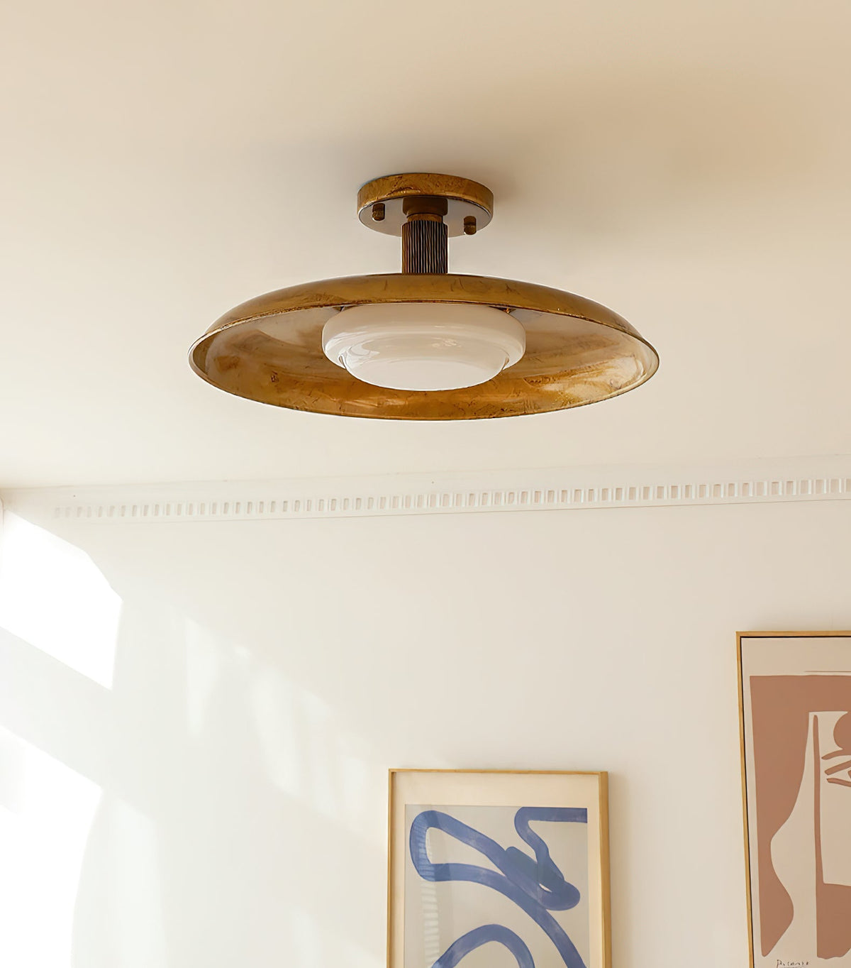 Gilded iron ceiling light beside a framed print on a cream wall — Casa Norex