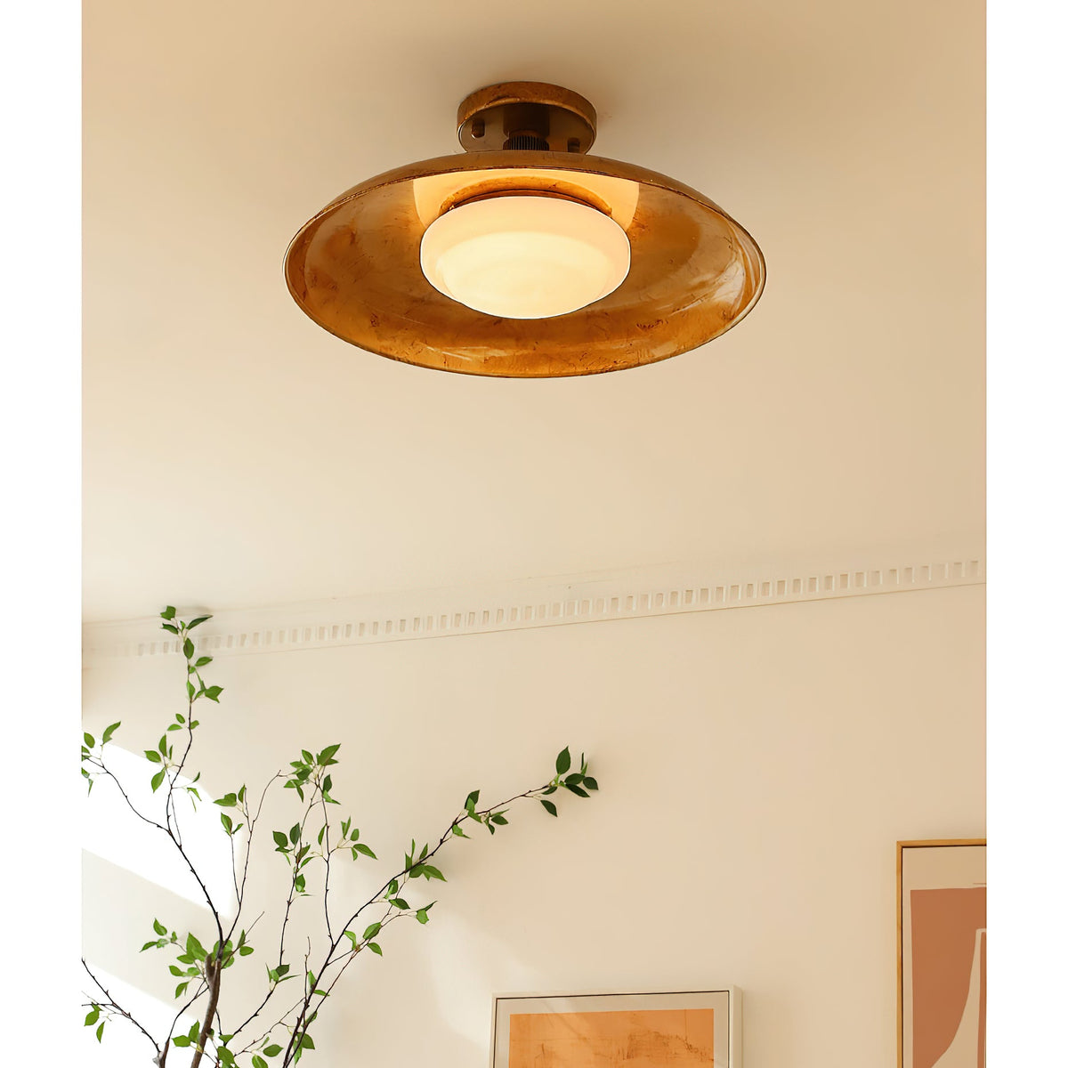 Gilded iron ceiling light seen from below beside a green plant — Casa Norex