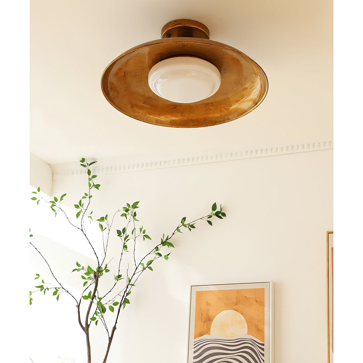 Gilded iron ceiling light glowing warmly above a plant branch — Casa Norex