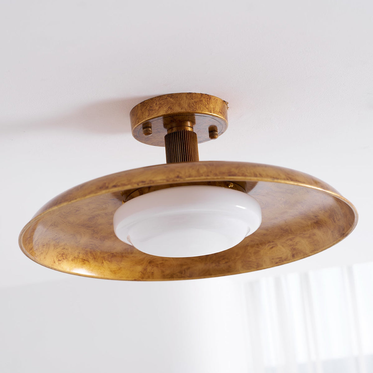 Wide gilded iron ceiling light with a glowing glass diffuser, angled view — Casa Norex