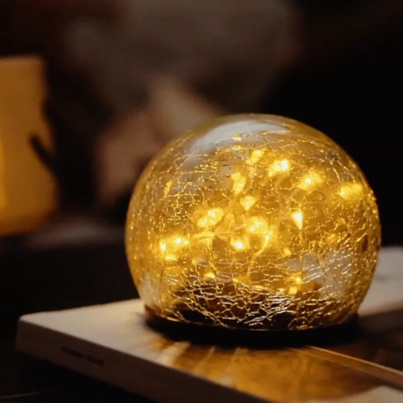 Close-up of a cracked glass globe with warm white lights inside — Casa Norex