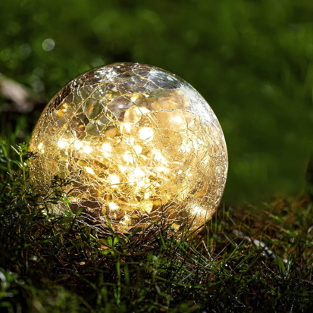 Cracked glass solar globe glowing on a lawn at dusk — Casa Norex