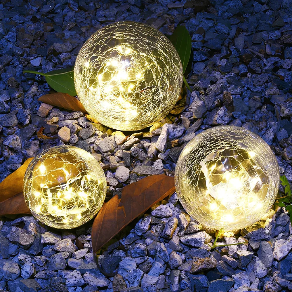 Three cracked glass solar globes on blue gravel — Casa Norex